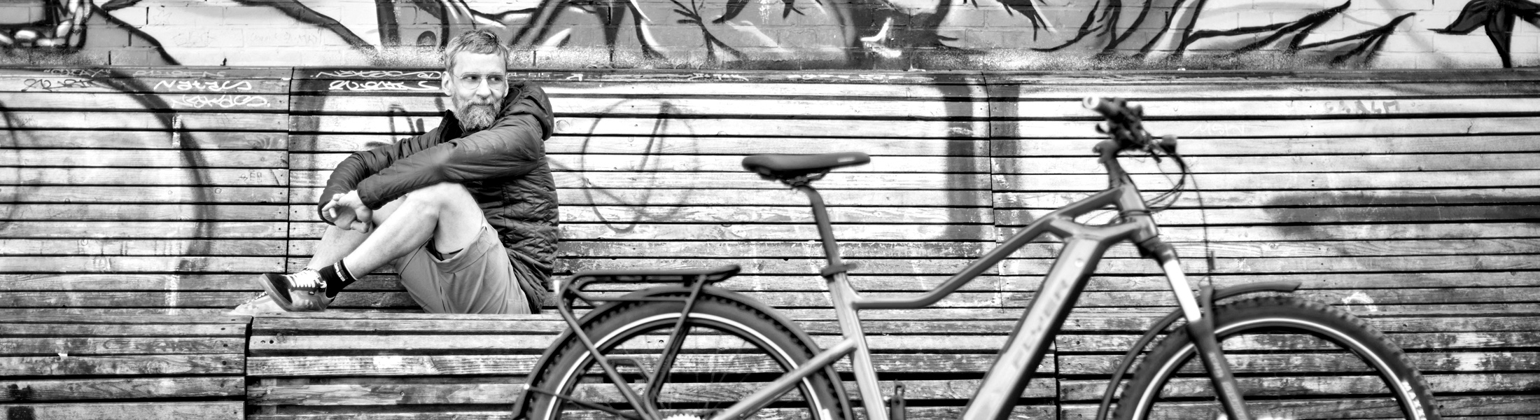 Mitarbeiter sitzt draussen auf einer Bank, davor ein E-Mountainbike